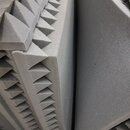 Šedé akustické pěnové panely s pyramidovitou strukturou. Panely jsou naskládány na sebe a mají matný povrch. Na fotografiích nejsou žádné viditelné z…
