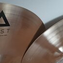 Detailní pohled na dva mosazné činely s broušeným povrchem. Na levém činelu je černý trojúhelníkový symbol a nápisy XIST a 14" Brilliant Hi-Hats. Pra…