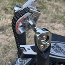 Detailní pohled na kovový mechanismus bubenového pedálu s černým řetězem. Na chromovaném členu je červený nápis POWER GLIDE a na spodní základně čern…