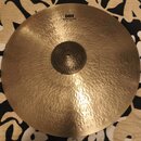 Zlatavý kovový činel s výrazně kovaným povrchem a matným vzhledem. V horní části je nápis HH Raw Bell Dry Ride 21"/53 cm. Uprostřed se nachází tmavší…