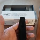 Černý nátrubek z tvrdého materiálu držený v ruce. V pozadí je otevřená kartonová krabice s nápisy D'Addario, SELECT JAZZ a textem popisujícím vlastno…