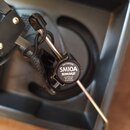 Detailní záběr na dynamický mikrofon s černým tělem a kovovým držákem. Na černé krytce je bílý nápis PATENTED SM10A SHURE A ASSEMBLED BY SHURE IN MEX…