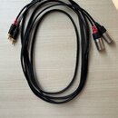 Dva černé audio kabely s konektory typu XLR na jedné straně a RCA na druhé. Na kabelích je vidět bílý nápis AUDIO CABLE a MODEL. Konektory RCA jsou v…