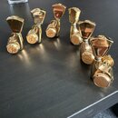 Šest zlatých ladicích kolíků z kovu s lesklým povrchem. Na spodních knoflících je hnědý kruhový štítek s nápisem „Gotoh“. Na bočních částech některýc…