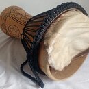 Djembe s dřevěným korpusem v přírodní barvě, který je zdoben řezbami. Membrána je z bílé kůže s viditelným chlupem po okrajích a je natažená pomocí č…