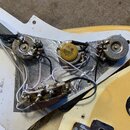 Detail vnitřní elektroniky elektrické kytary s bílým plastovým krytem a kovovou stíněcí vrstvou. Jsou vidět tři potenciometry a jeden kondenzátor s n…