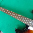Elektrická kytara s černým bodies, hnědým hmatníkem a bílým pickguardem. Na hlavě je vidět nápis "STRAT". Hmatník má bílé tečkové značky a viditelné…