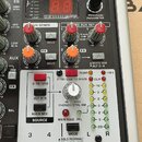 Detailní pohled na ovládací panel mixážního pultu s digitálním displejem, který zobrazuje červené číslice 8.8. Na panelu jsou vidět různé ovladače, č…