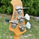 Zadní strana hlavy basové kytary z vyvrtaného světlého dřeva. Na dřevě je nápis MADE IN SAN LUIS OBISPO CALIFORNIA, USA. Jsou zde čtyři kovové ladičk…