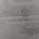Detailní záběr na šedý plastový povrch s vyraženým varovným textem v angličtině, francouzštině a němčině. Text začíná slovy CAUTION TO PREVENT ELECTR…