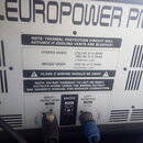 Detail zadní strany zesilovače s nápisem .EUROPOWER PMH. Na šedém kovovém panelu jsou vidět tři výstupy pro reproduktory s popisky RIGHT/MONO MAIN, B…