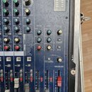 Detailní pohled na ovládací panel modrého mixážního pultu v rackovém pouzdře. Panel obsahuje zahlreiche otočné knoflíky, posuvníky a přepínače s nápi…