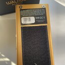 Záběr na spodní stranu zlatého efekt pedálu. Na horní části je nalepený bílý štítek s textem „THIS DEVICE COMPLIES WITH PART 15 OF THE FCC RULES...“,…
