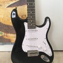 Černá elektrická kytara s bílým pickguardem a hnedým hmatníkem. Nástroj má tři snímače typu single-coil, jeden přepínač a tři bílé oválné knofíky s n…
