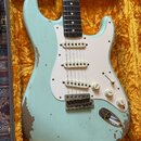 Světle modrá elektrická kytara typu Stratocaster s bílým pickguardem a třemi snímači. Tělo vykazuje výrazné opotřebení laku, zejména v dolní části a…
