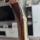 Detailní pohled na hmatník a krk kytary z tmavého dřeva se světlým lemováním. Na horní části je vidět kovový ladicí kolík a struna. Povrch dřeva vyka…