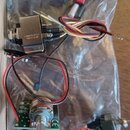 Na průhledném plastovém sáčku leží elektronické součástky s dráty v různých barvách. Je zde kovový přepínač s nápisem KEYSTONE ELECTRONICS a potencio…
