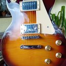 Elektrická kytara s trupem v červeně-žlutém sunburst provedení a krémovým pickguardem. Nástroj má dva humbuckery s kovovými kryty, chromovaný kobylní…