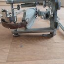 Detailní pohled na kovový mechanismus bicího pedálu v stříbrné barvě. Na beateru je vidět výrazně opotřebovaná a potrhaná hnědá kožená nebo syntetick…