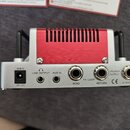 Zadní strana stříbrného kytarového zesilovače s červeným chladičem. Jsou zde vidět konektory a nápisy 18V DC, LINE OUTPUT, AUX IN, FX LOOP SEND, RETU…
