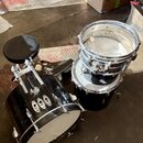 Sada černých bubnů z bicího setu včetně basového bubnu, tom-tomu a malého bubnu. Nástroje mají chromované obruče a mechanismy, povrch vykazuje vidite…