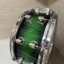Zelený snare drum s glitrovým povrchem a chromovanými obručemi a šroubnicemi. Nástroj nemá žádné viditelné značky, loga ani nápisy. Povrch je čistý a…