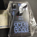 Černý kytarový zesilovač v plastovém obalu. Na zařízení jsou nápisy VOLUME, TC-3, 3 WATT TRANSISTOR GUITAR POWER AMPLIFIER a velký nápis TUBE CAKE s…