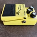 Žlutý efekt pedál s černým spínacím tlačítkem. Na horní straně je nápis SUPER OverDrive SD-1 a u tlačítka značka BOSS. Zařízení má tři černé ovládací…