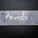 Detailní záběr na šedý obdélníkový štítek. Na štítku je bílým kurzívním písmem nápis Fender a v pravém dolním rohu černým tiskacím písmem nápis TELEC…