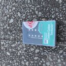 V průhledném plastovém obalu je umístěn elektrický kytarový snímač typu humbucker s černým plastovým krytem a viditelnými bílými pólky. Na krytu je b…