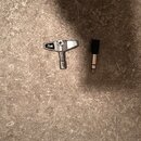 Na fotografii jsou dvě součásti kabelu položené na šedém povrchu. Vlevo je kovový konektor s nápisem Pearl, vpravo je černý plastový kryt s kovovým h…