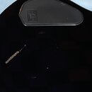 Detail černého povrchu hudebního nástroje s kovovým krytem v horní části. Na krytu je viditelné logo, které je však nečitelné. V levé části černého p…