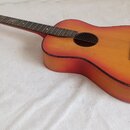 Akustická kytara s červeně-oranžovým přechodem barvy (sunburst). Nástroj nemá žádné viditelné značky, loga ani nápisy. Povrch vykazuje známky opotřeb…