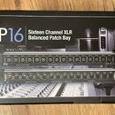 Fotografie znázorňuje krabici s produktem P16 Sixteen Channel XLR Balanced Patch Bay. Na obalu jsou zobrazeny dvě černé rackové jednotky s řadou XLR…