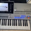 Stříbrošedý digitální klavír s nápisy YAMAHA a Tyros 5. Nástroj má velký displej, na kterém je zobrazen text Tyros 5 a v dolní části nápis © 2012 YAM…