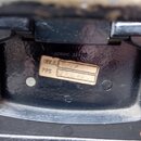 Detail vnitřní části černého kufru z texturovaného materiálu. Na povrchu je nalepená vybledlá papírová nálepka s nápisy INV.č., PPS a ručně dopsanými…