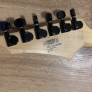 Detail hlavy světlé dřevěné kytary s šesti černými ladicími kolíky. Na zadní straně hlavy je černý nápis s logem CE RoHS, textem SERIAL NUMBER 140103…