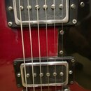 Detail červené elektrické kytary se dvěma humbuckery s chromovanými kryty. Na obou snímačích je nápis Tuwa. Pod snímači je vidět chromovaný kobylník.…