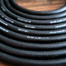 Detailní záběr na smotaný černý kabel s bílým nápisem. Na povrchu jsou viditelné texty CANARE, L-2T2S, 1805 a MADE IN JAPAN. Povrch kabelu je matní a…