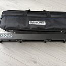 Černý textilní obal a černý kovový stojan s nápisy ROCKBOARD® by WARWICK. Na pravé straně stojanu je uveden model DUO 2.2. Obě věci jsou umístěny na…