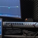 Stříbrné rackové audio rozhraní s řadou ovládacích knoflíků a vstupních konektorů. Na levé straně je vidět nápis "Cusom". Do jednoho ze vstupů je zap…