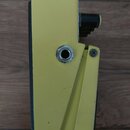 Žlutý efekt pedál z kovového materiálu. Na boku je viditelný vstupní jack konektor a část černého ovládacího knoflíka. Povrch laku vykazuje drobné šk…