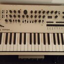 Světle šedý polyfonní analogový syntetizátor s klávesnicí. Na předním panelu je nápis KORG minilogue POLYPHONIC ANALOGUE SYNTHESIZER. Zařízení obsahu…
