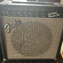 Kytarový kombo zesilovač v černém obalu s hnědou textilní maskou. Na horním ovládacím panelu jsou nápisy Sidekick Reverb 30 a Fender Musical Instrume…