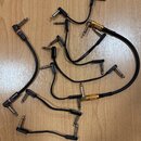 Sada černých propojovacích patch kabelů s 6,3mm jack konektory. Některé kabely mají zlaté kovové prstence a jiné jsou vybaveny červenými nápisy, z ni…