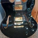Černá polodupatá elektrická kytara s gold hardwarem a dvěma f-otvory. Nástroj má dva humbuckery, zlatý kobylník a čtyři ovládací knoflíky. Povrch je…
