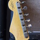 Zadní strana hlavy kytary zC světlého dřeva s šesti kovovými ladicími mechanismy. Na dřevě je vidět logo s nápisem Fender Custom Shop v trojúhelníkov…