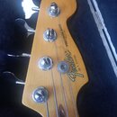 Detail hlavy basové kytary z přírodního dřeva s nápisem Fender Precision Bass MADE IN USA. Na dřevě je vidět sériové číslo E 319100 a nápis SERIAL NU…