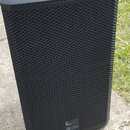 Černý aktivní subwoofer s kovovou perforovanou mřížkou a texturovaným povrchem skříně. V pravém dolním rohu je bílé logo s nápisem dB technologies a…