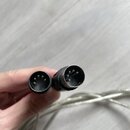 Fotografie zachycuje dva konce kabelu s konektory typu XLR. Konektory jsou černé, z plastu a kovu, s viditelnými vnitřními piny. Povrch konektorů vyk…